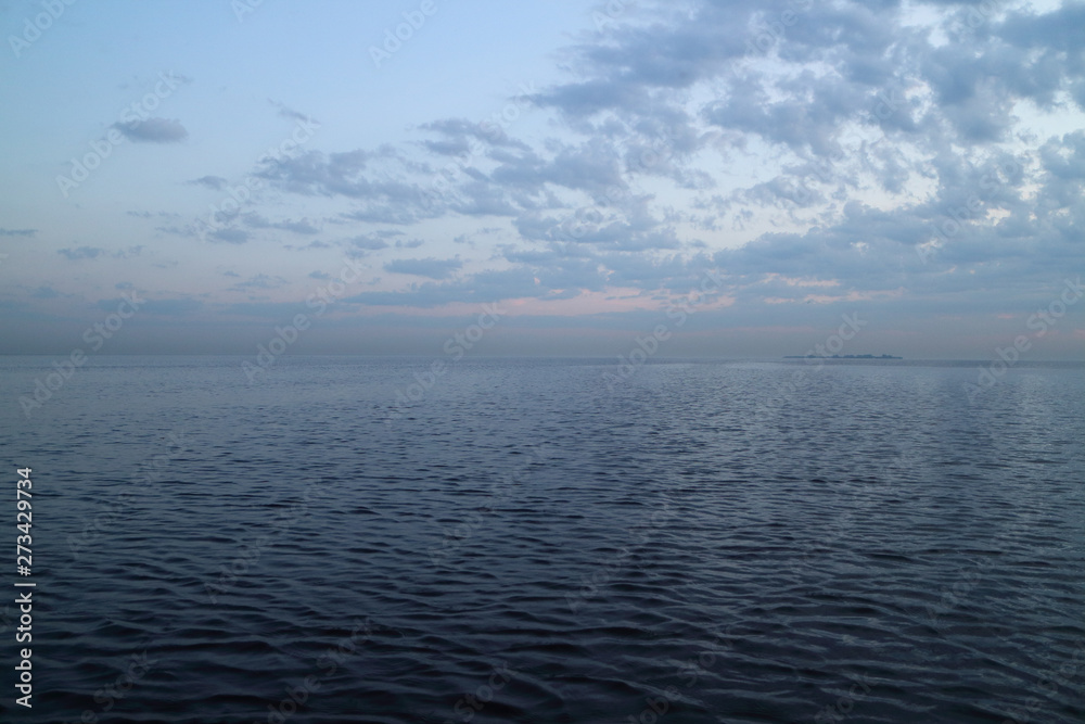 Obraz premium sunset at sea, sun beyond the clouds, seascape island on the horizon