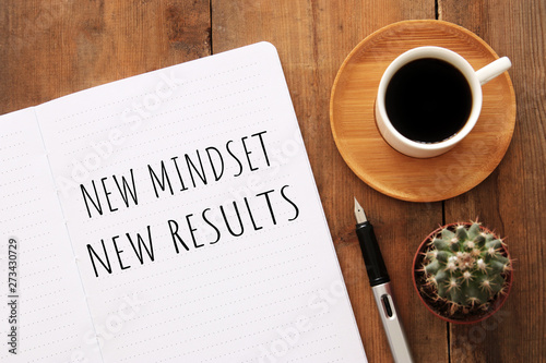 Photo top view image of table with open notebook and the text new mindset new results