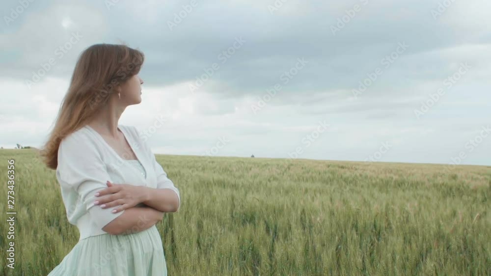 Beautiful young russian girl among the tall green spikelets of wheat in the field. Young woman enjoying summer, harmony of human and nature, health and solitude Beautiful young russian girl among the tall green spikelets of wheat in the field. Young woman enjoying summer, harmony of human and nature, health and solitude
