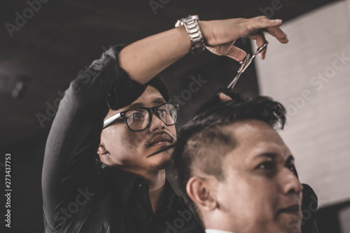 Portrait of barber making hair cut of his attractive man in barbershop