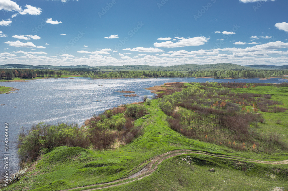 Panoramic footage of Russia nature; lake surrounded by birch pine trees, spring green meadows; forest mountains in the background; leaves swaying in the wind; aerial view; drone flying over a river