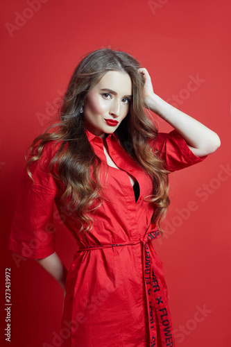 Fashion portrait of woman in red dress, beautiful makeup, curly long hair. Girl perfect lip makeup on red background