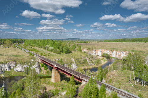 Aerial view; drone flying over the old railway bridge crossing the river; dense vegetation on the banks of the river; beautiful picturesque road; transportation through the landmarks