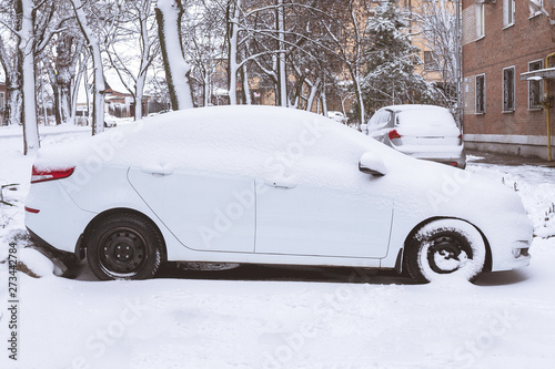 white car covered with snow parked near the house. snowstorm fell asleep car. © Ilya_R