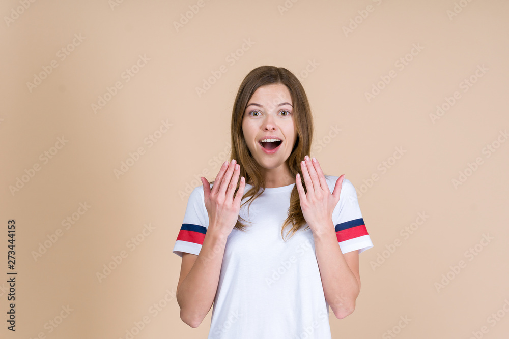 Young excited woman standing on pastel beige background and holding palm hand near face Young excited woman standing on pastel beige background and holding palm hand near face