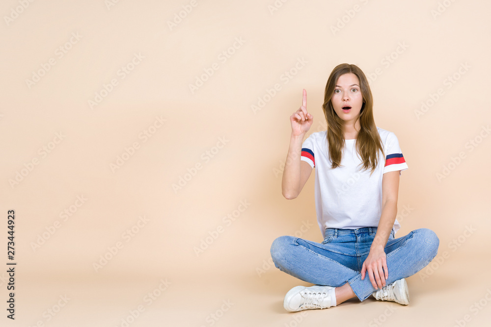 Young woman with crossed legs sitting on pastel beige background Young woman with crossed legs sitting on pastel beige background
