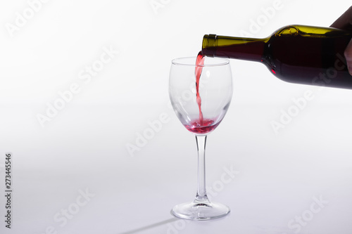 Red wine pouring from bottle into big glass on white background with copy space