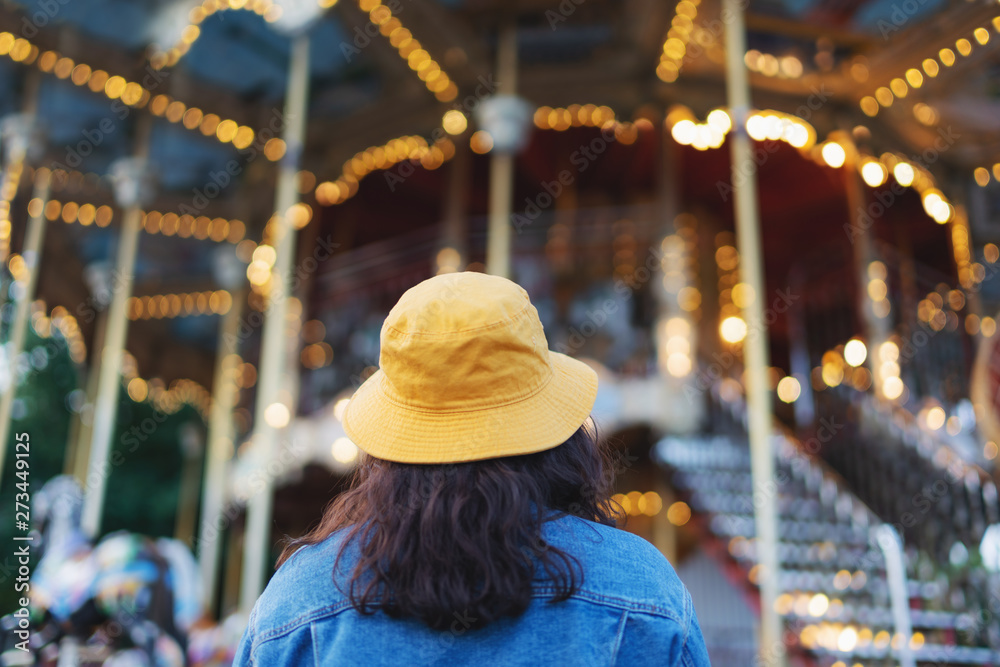 Young woman in yellow hat looking at roundabout in theme-park in summer Young woman in yellow hat looking at roundabout in theme-park in summer