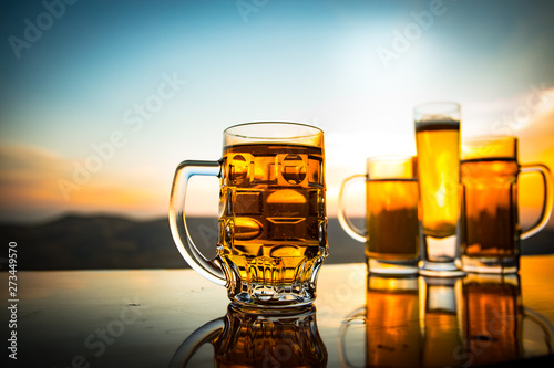 Glass of beer on a beach at sunset. Cooling summer drink concept. Close Up of A Glass of Draught Beer with the Bokeh of Sunlight Background