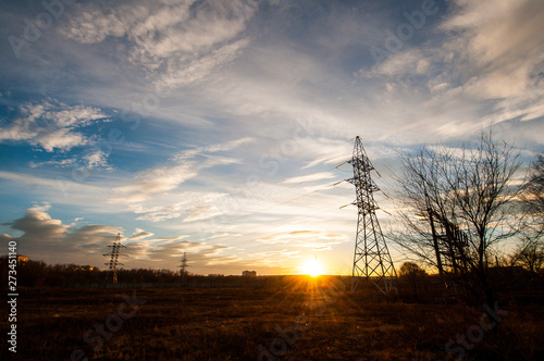 electric transmission lines in the field near the city in the rays of a beautiful bright yellow sunset
