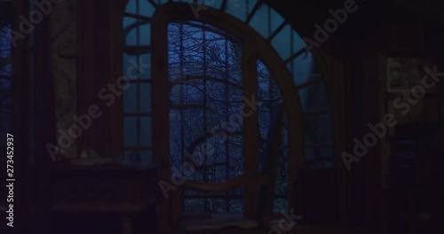 Old creepy window of a scary haunted house overlooking a haunted forest with trees moving in the wind. Old objects in old solid wood, old wallpaper damaged, changing focus. Shot on red epic 6K.