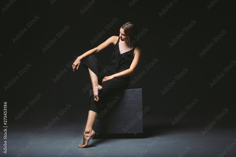 Social theme. young Caucasian woman in strange pose in dress posing on black cube, dark background, symbolizes pain, suffering, seeking help, protection of an evil society. Modern art, abstraction