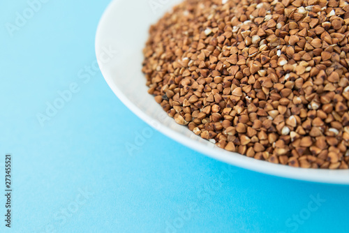 Plate with raw buckwheat on a blue background