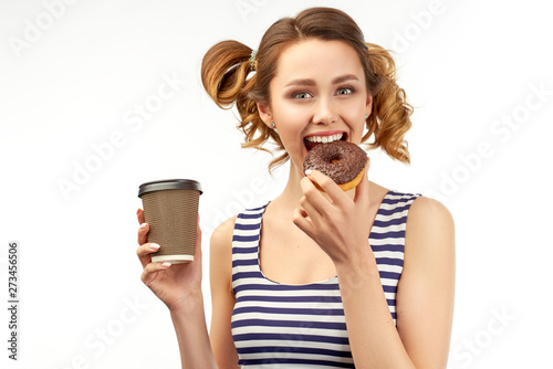 Happy girl in a striped t-shirt holding a donut and a drink. Funny cute expression of a young sweet tooth. She biting a chocolate donut. The concept of a quick and tasty snack