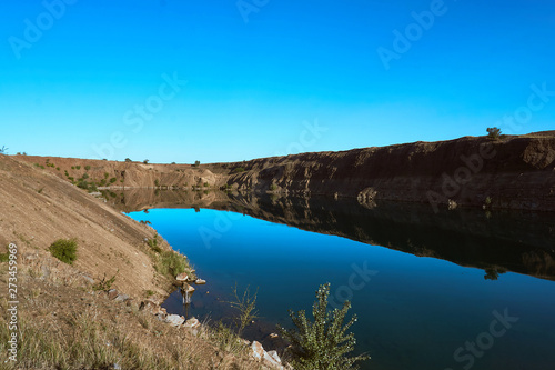 an amazing wild lake without people in a gorge of sand color among the stones and trees with crystal clear blue water on a nice warm summer day in the bright sun
