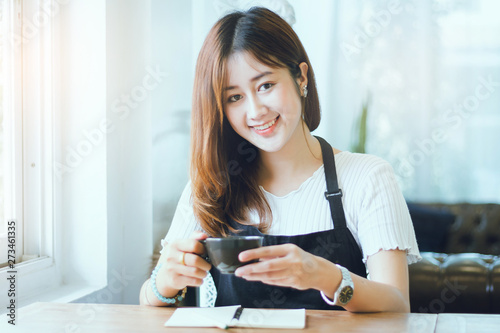 Portrait of young beautiful woman holding cup of coffee with notebook on wooden table in cafe