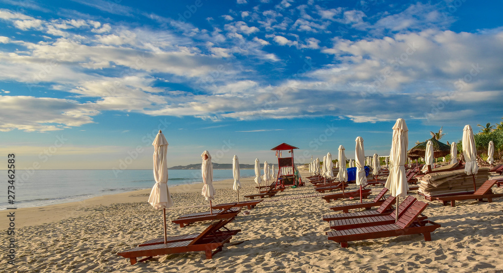 Sun loungers and umbrellas on an empty sandy beach. Summer sunny cloudy blue sky. Cam Ranh. Vietnam.