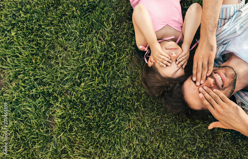 Top view image of happy handsome father and cute child playing in the park. Horizontal above view portrait of dad and his adorable little girl covering their eyes with hands playing peek-a-boo photo