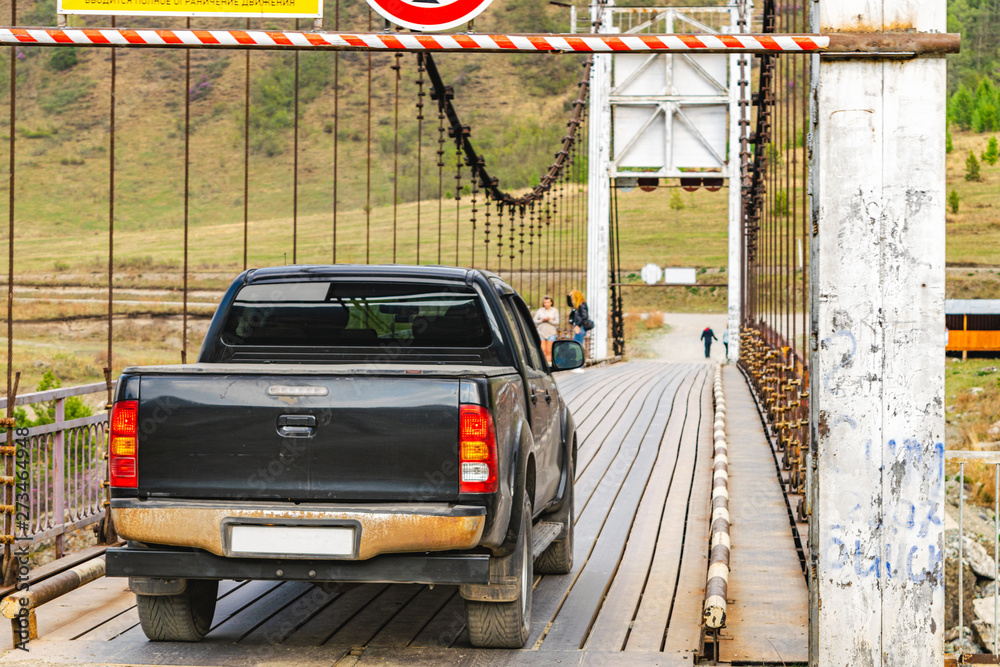 Naklejka premium Pickup truck passing over a suspension bridge over a mountain river
