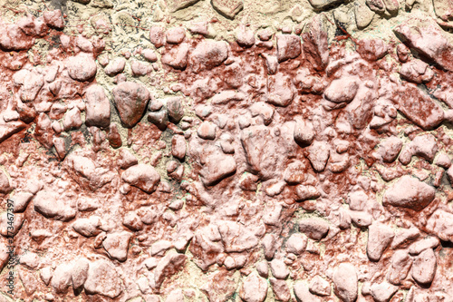 Stone rubble in a concrete wall painted with red paint as a background
