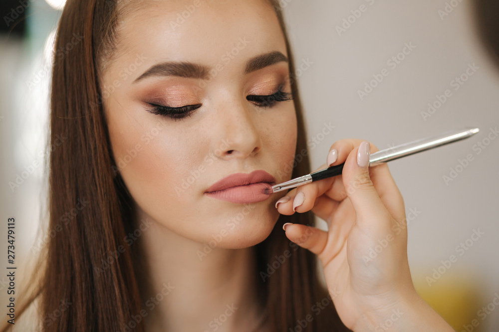 Makeup artist applies lipstick. Hand of make-up master, painting lips of young beauty redhead model. Make up in process. Closeup view