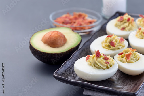 Deviled eggs stuffed with avocado, egg yolk and mayonnaise filling, garnished with bacon, horizontal, copy space