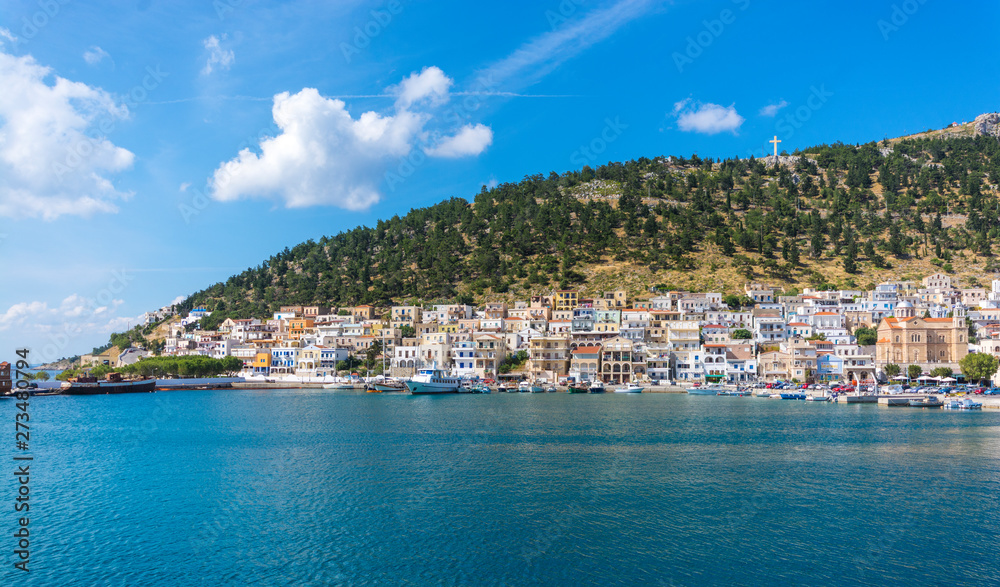  view at the sea at the shore and colored houses on the beach against the green hills with trees on the island of Kalymnos in Greece