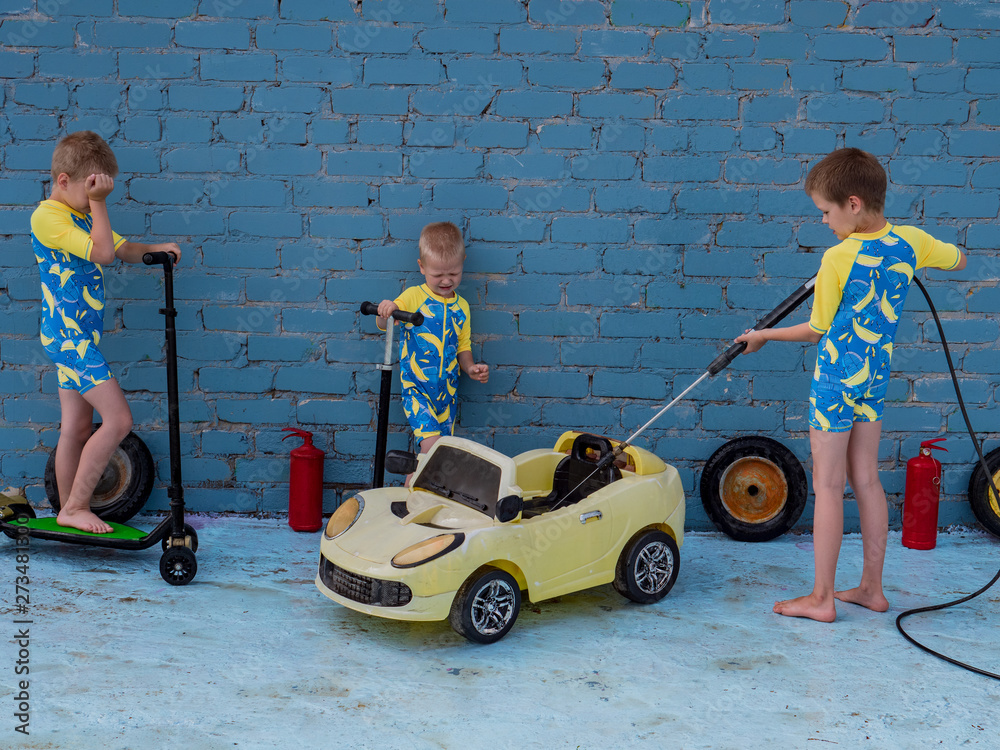 Funny children in boys' bathing suits posing in front of camera with high-pressure car wash and toy yellow car and scooters. Brothers are trying to wash car. Concept educational games for preschoolers