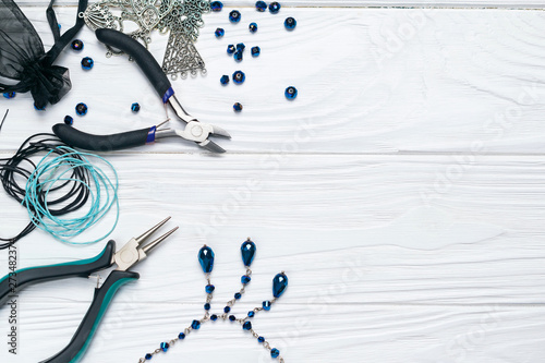 Jewelry findings handmade craft composition with pliers beads embellishments and necklace on white wooden background photo