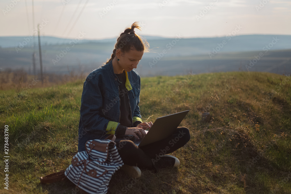 young girl working at laptop with earphones in the fields 