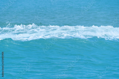 Bubbles of sea waves on the bright blue water surface.