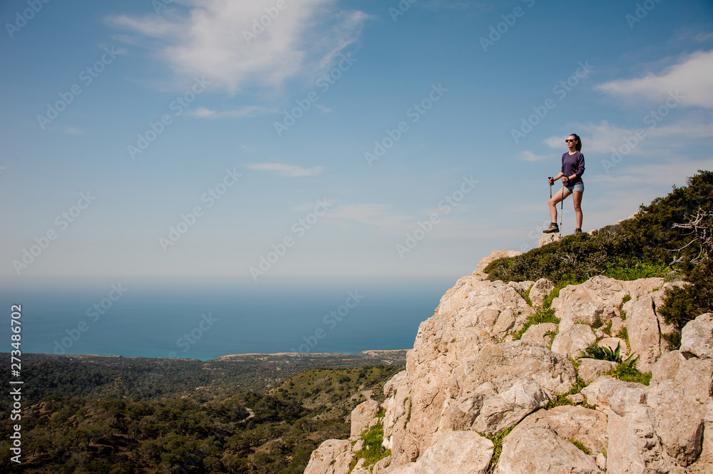 Girl standing on the rock in shorts with walking sticks