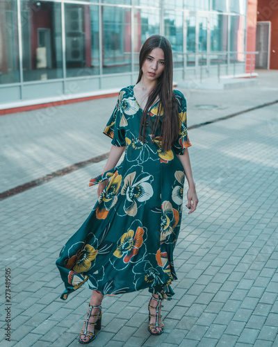 Beautiful girl model posing against the background of the glass building in a wonderful dress.