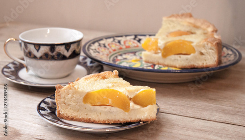 Slice of peach apricot pie or cheese sour cream cake on bright saucer with tea cup on wooden table