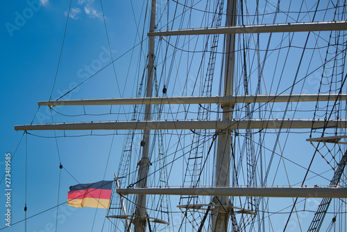 rigging and masts of a big sailing ship in front of a blue sky with the black-red-golden flag of the state Germany, ship