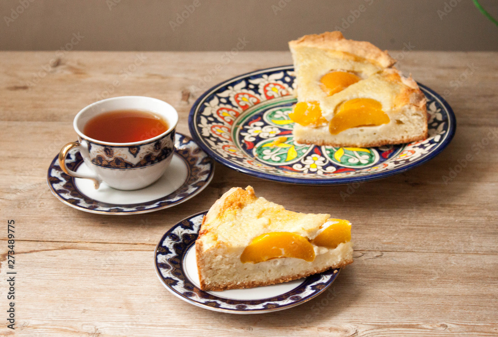 Slice of peach apricot pie or cheese sour cream cake on bright saucer with tea cup on wooden table