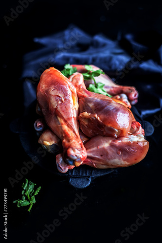 Raw cut unwashed chicken drumsticks in a steel plate isolated in black along with some fresh parsley or coriander leaves on it. Vertical close up shot. photo