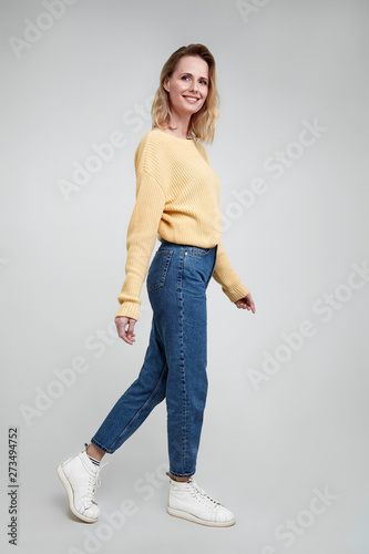 Slim and beautiful. Full length studio shot of attractive young woman in casual wear keeping hand on the air and smiling walking against grey background