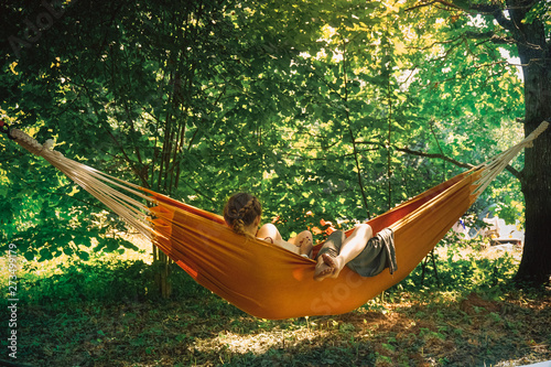Woman relaxing in the hammock in the middle of a forest, watching sundown. Slow life concept. Hipster.