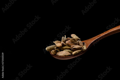 Cardamom seeds on wooden spoon over black background. 
