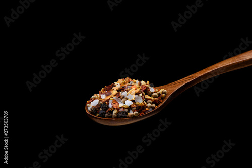 Mixture of spices for culinary mill on wooden spoon over black background.