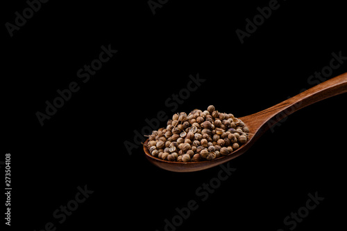 Coriander seeds on wooden spoon over a black background.