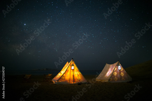 Camping under stars, night sky in the desert, the Milky Way, tents glowing from the inside. Vacation holidays in nature. Sleep under sky