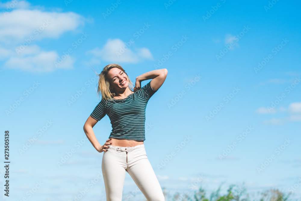 Happy beautiful slim athletic girl with a beautiful smile in white tight pants against the blue sky. Happy beautiful slim athletic girl with a beautiful smile in white tight pants against the blue sky.