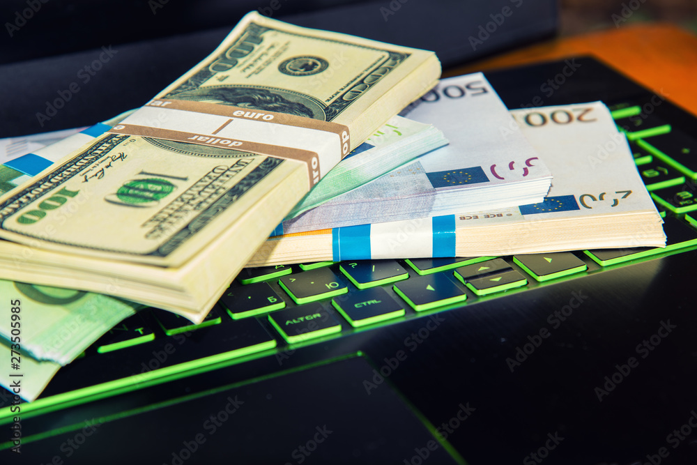 Money on a laptop, bundles of dollars and euros are on the keyboard of a laptop, the concept of online wages and the Internet win. Money on a laptop, bundles of dollars and euros are on the keyboard of a laptop, the concept of online wages and the Internet win.