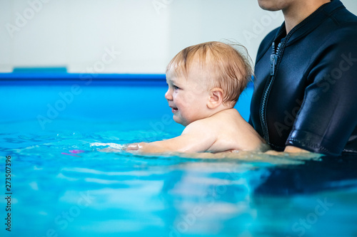 Cute sad baby boy learning to swim in special pool for little children