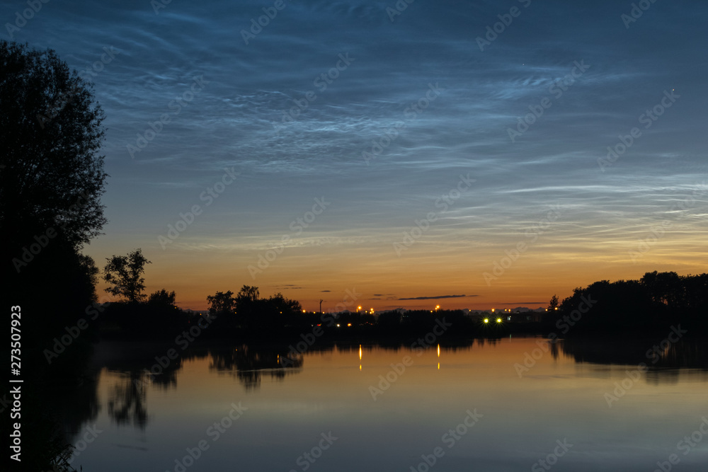 Obraz premium Noctilucent clouds over northwestern Europe, seen from the shore of a lake at night on a calm night
