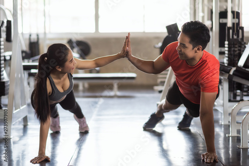 Young Asian sporty couple sit up exerise together at gym, Fitness man and woman giving each other a high five during the training session in gym. Sport and healthy lifesytle.