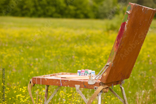 Outdoor shot, photo in open air, old sketchbook over green meadow background, artist's equipments, beautiful nature with yellow flowers on green grass, painters' tools on against forest and meadow. photo