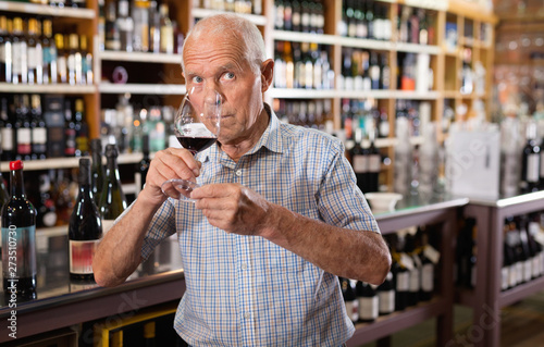 Confident elderly man tasting red wine in wine store before buying